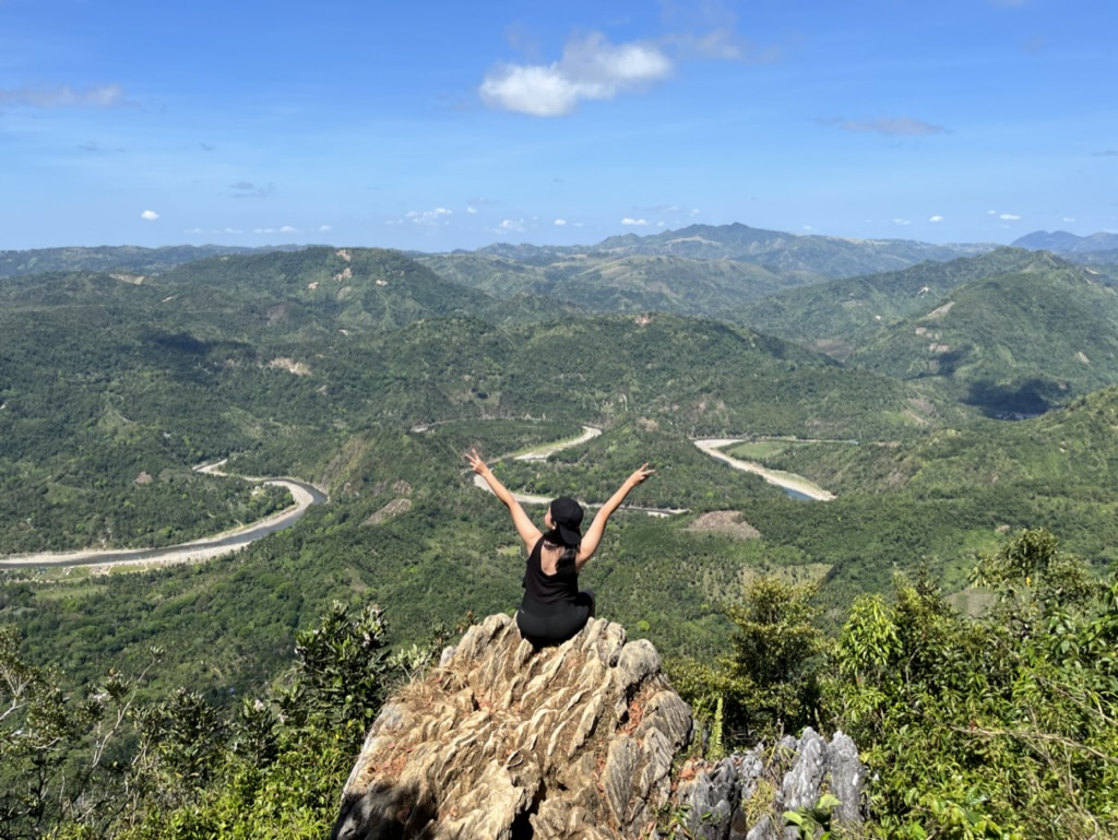 Pam sitting on a mountain summit with arms raised