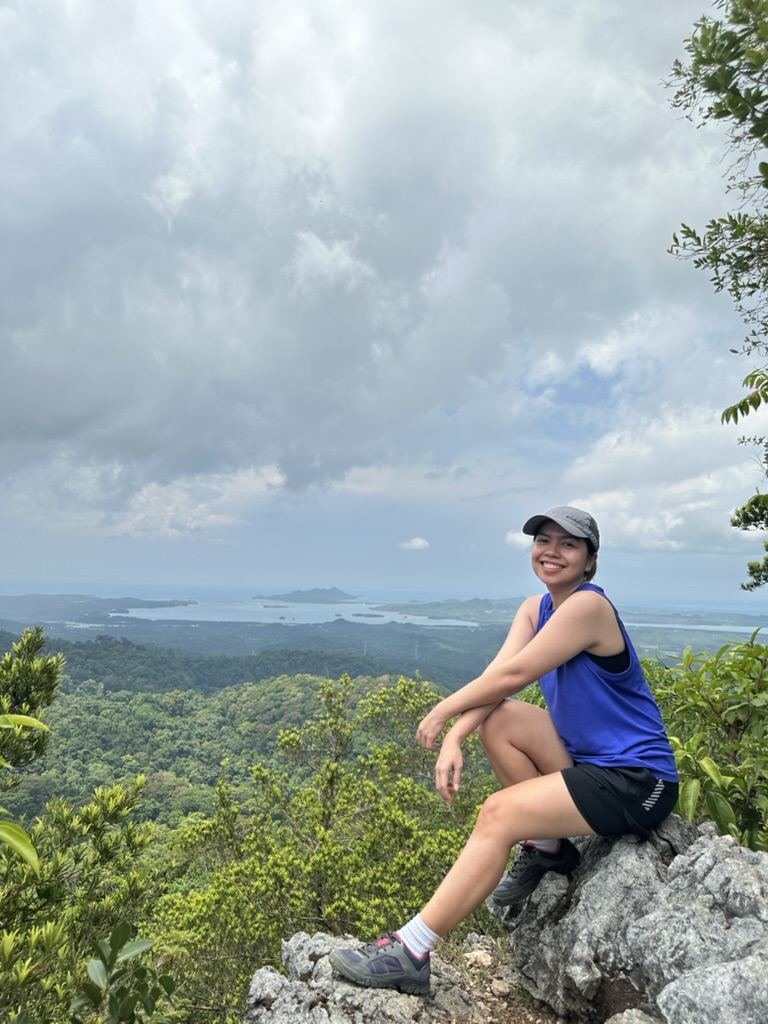 Pam smiling on a mountaintop overlooking the coast