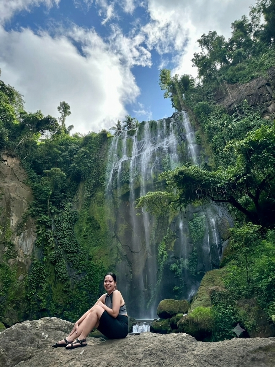 Pam seated on rocks in front of a lush jungle waterfall
